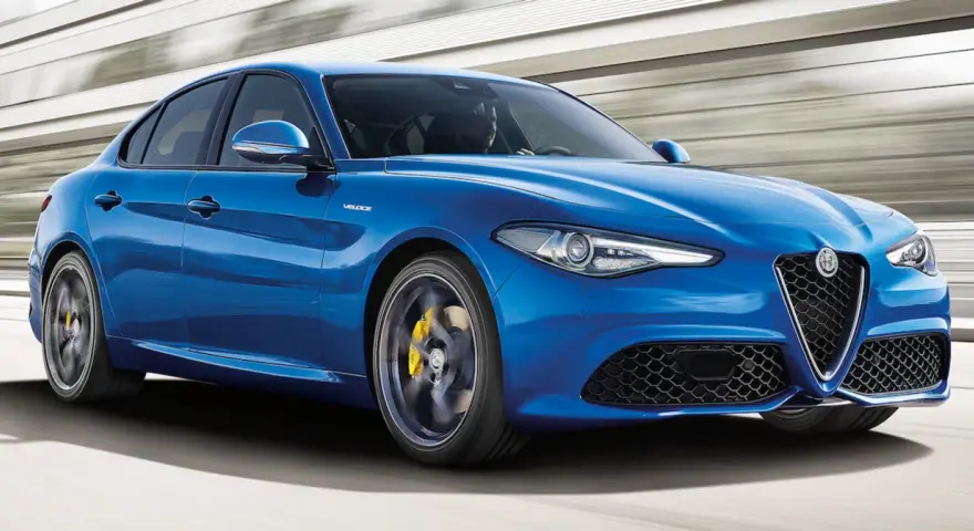 Błękitne Alfa Romeo Giulia Veloce pędzi po drodze, ukazując sportowy charakter i dynamiczną sylwetkę.