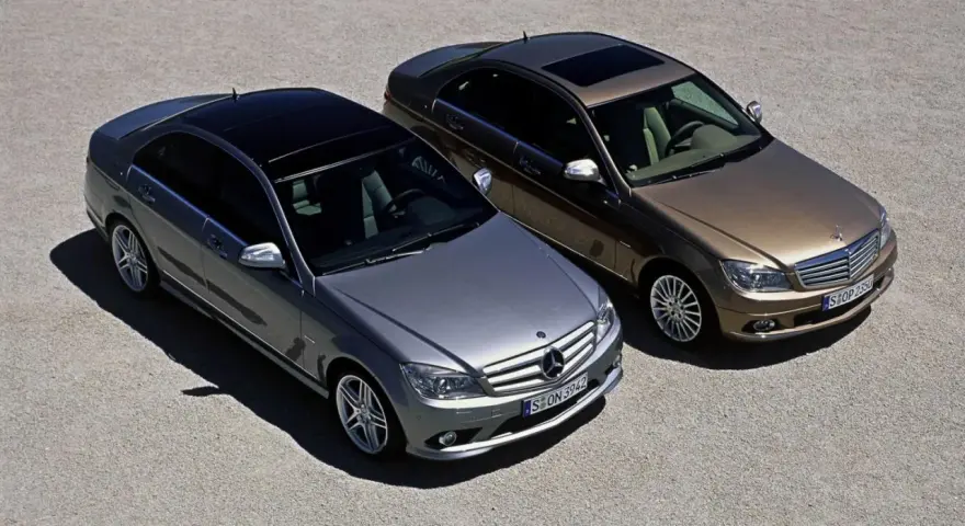 Dwa Mercedesy klasy C W204, jeden srebrny, drugi brązowy, stoją obok siebie na żwirowym placu.