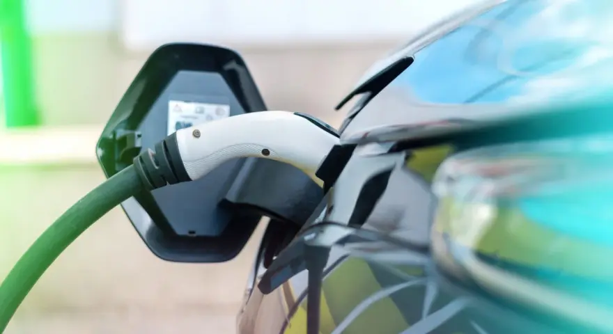 Ładowanie samochodu elektrycznego. Wtyczka podłączona do portu ładowania, zielony kabel biegnie do stacji.
