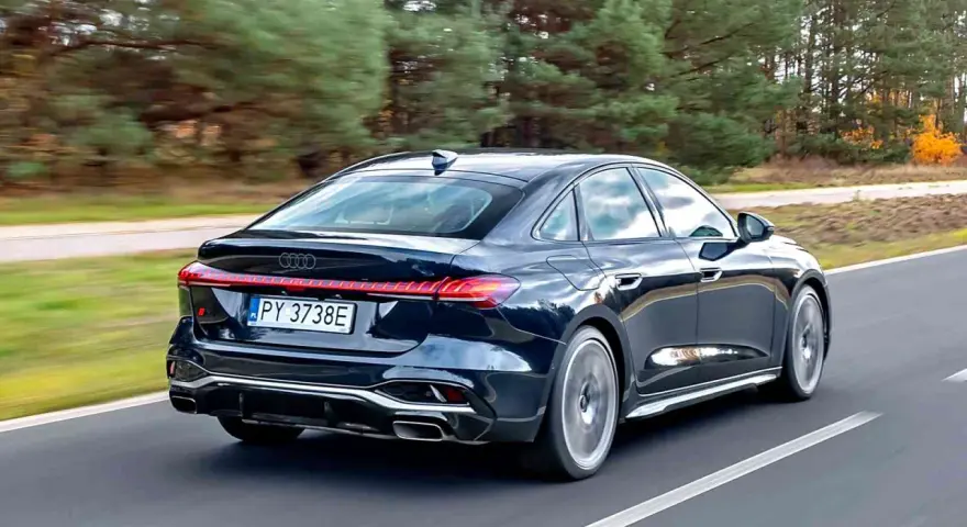 Ciemny Audi A4 B10 pędzi po drodze, otoczony jesiennym lasem.