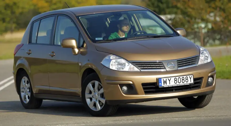 Złoty Nissan Tiida z mężczyzną za kierownicą jedzie po drodze.