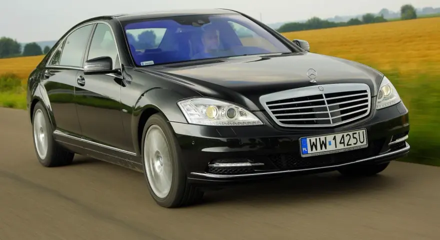 Czarny Mercedes-Benz W221 pędzi po drodze, mijając pola.