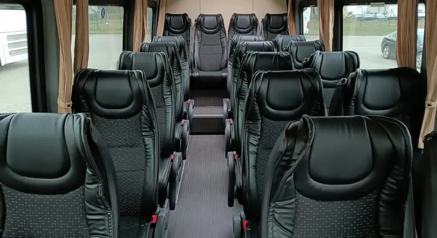 Wnętrze busa z rzędami czarnych, wygodnych siedzeń. Widać, ile miejsc ma bus osobowy, gotowy na podróż.