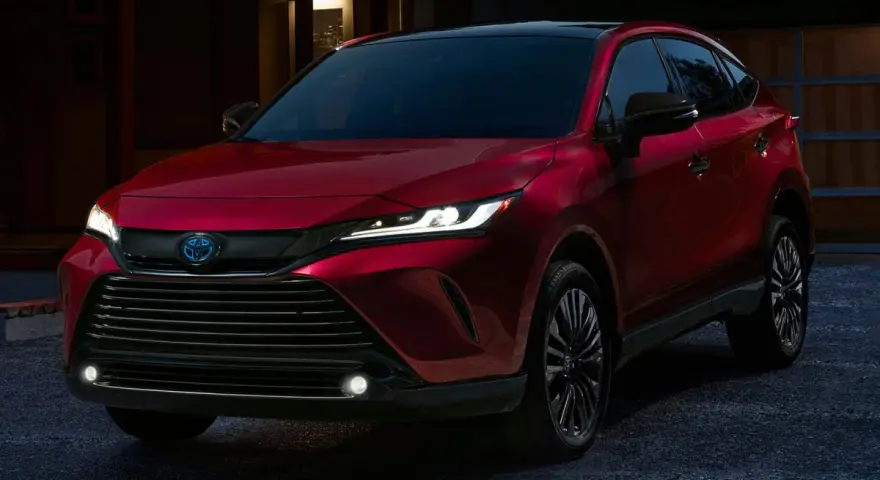 Elegancka, czerwona Toyota Venza z nowoczesnymi światłami LED stoi przed domem o zmierzchu.