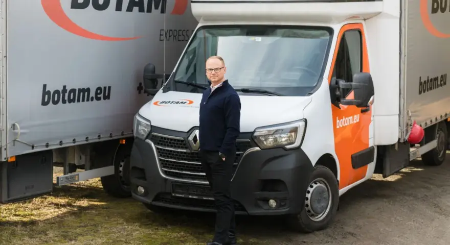 Mężczyzna stoi przed białym busem do transportu międzynarodowego marki BOTAM.