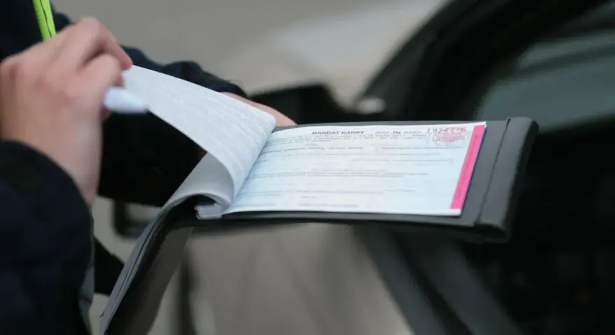 Policjant wypisuje mandat za kolizję. Dokument zawiera numer seryjny i pieczęć.