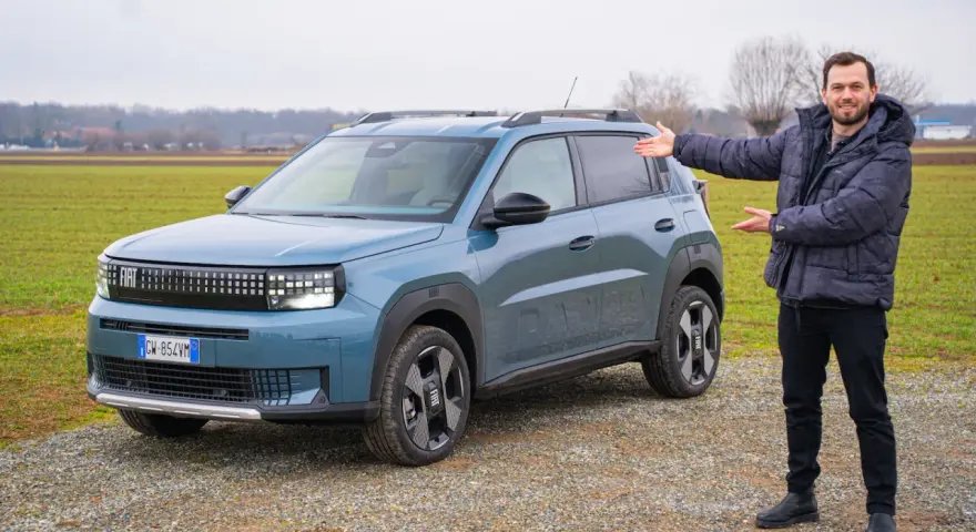 Mężczyzna prezentuje nowy, niebieski Fiat Grande Panda na tle zielonego pola.