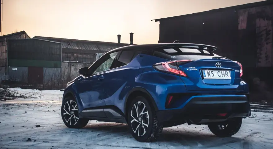 Niebieska Toyota C-HR Hybrid na tle opuszczonych budynków. Czy wybrać hybrydę czy benzynę?