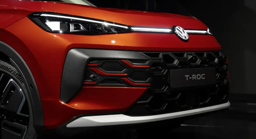 Nowy VW T-Roc w kolorze pomarańczowym prezentuje się z przodu z charakterystycznym grillem i nowoczesnymi światłami IQ.LIGHT.