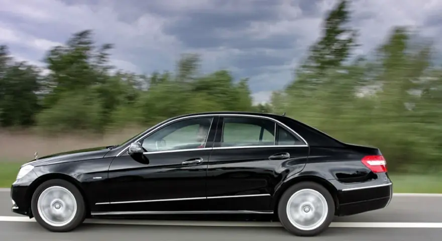 Czarny Mercedes E350 pędzi po drodze, mijając rozmyte zielone drzewa.