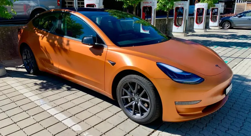 Pomarańczowa Tesla Model 3 na ładowarce. Zastanawiasz się, ile przejedzie Tesla na jednym ładowaniu?