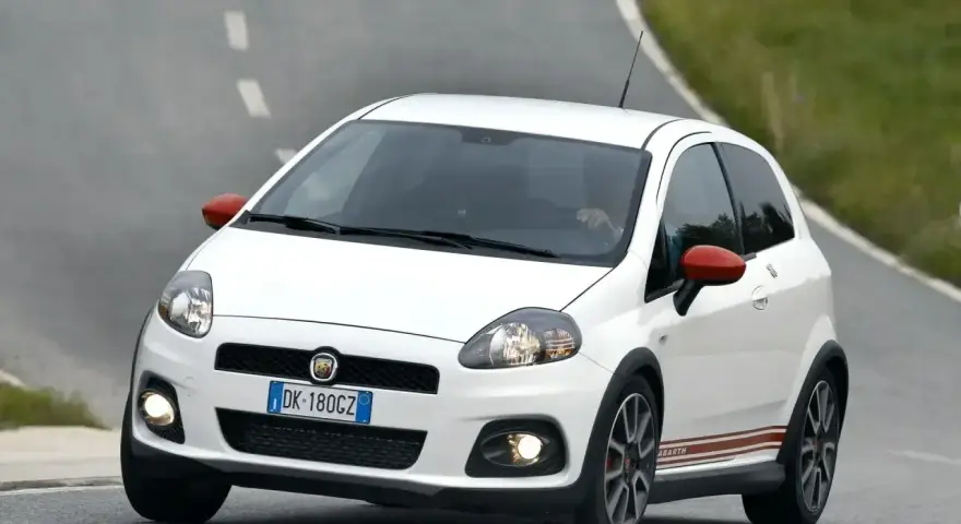 Biały Fiat Punto Evo Abarth z czerwonymi lusterkami pędzi po zakręcie drogi.