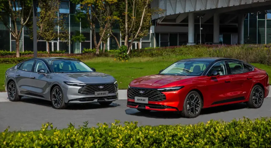 Dwa nowe Fordy Mondeo mk6, jeden czerwony, drugi szary, stoją obok siebie na tle nowoczesnego budynku i zieleni.
