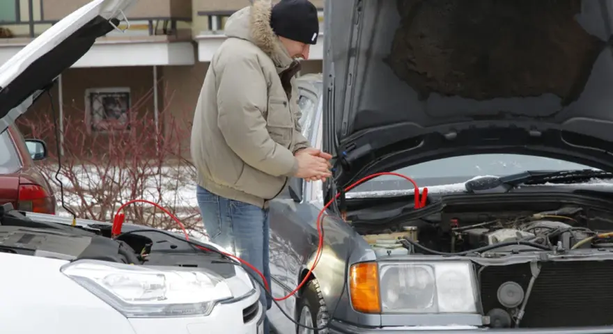 Mężczyzna podłącza kable rozruchowe do samochodu, by odpalić toyotę hybrydę na kable.