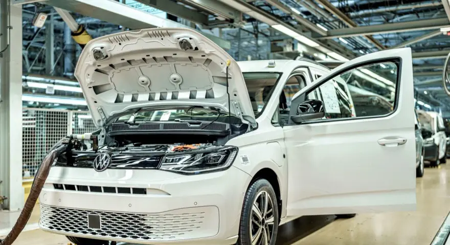 Biały samochód elektryczny na linii produkcyjnej. Widać otwartą maskę i drzwi, a także elementy silnika. Powstają tu polskie samochody.