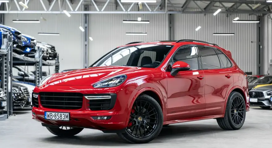 Czerwony Porsche Cayenne GTS lśni w salonie, gotowy na podbój dróg.