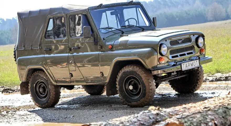 Zielony UAZ z plandeką, marka samochodu na u, pokonuje błotnisty teren.