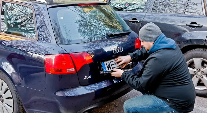 Mężczyzna montuje tablicę rejestracyjną na samochodzie Audi A4. Nowa rrs rejestracja gotowa do drogi.
