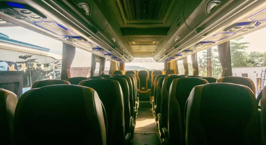 Wnętrze autobusu z rzędami zielonych siedzeń. Trudno ocenić, ile bus ma miejsc, ale wygląda na to, że jest ich sporo.