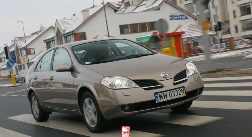 Brązowy Nissan Primera przejeżdża przez pasy na tle zaśnieżonych domów.