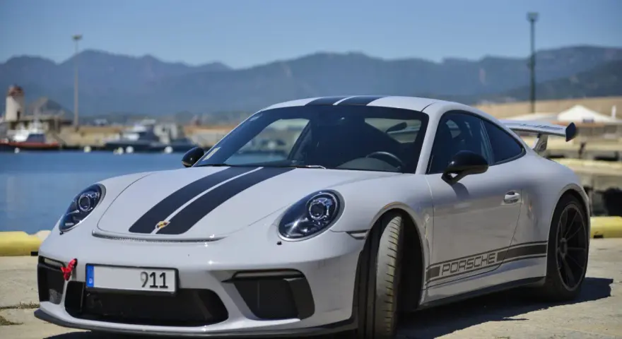 Szary Porsche 911 z czarnymi pasami, stojący nad wodą. Zastanawiasz się nad porsche 911 cena?