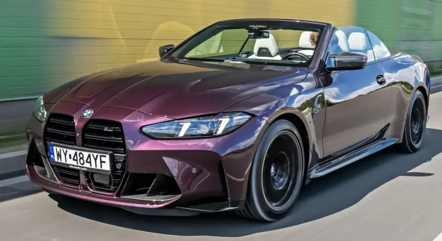 Fioletowe BMW M4 Competition kabriolet pędzi po drodze, odsłaniając białe wnętrze i sportowe detale.