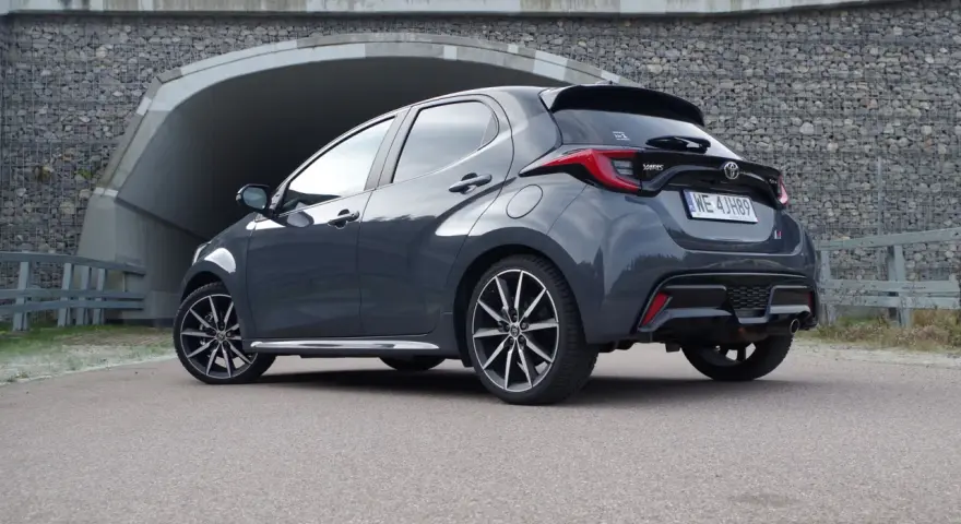Szary Toyota Yaris GR Sport z czarnym spojlerem i dyfuzorem, zaparkowany przed tunelem.