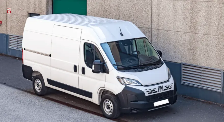Biały bus 9 osobowy Fiat Ducato, zaparkowany przy betonowej ścianie. Zastanawiasz się, ile pali bus 9 osobowy?