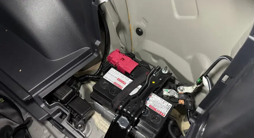 Akumulator 12V w Toyocie Prius znajduje się w bagażniku, pod plastikową osłoną. Widoczne są dwa akumulatory, jeden z czerwonym zabezpieczeniem.