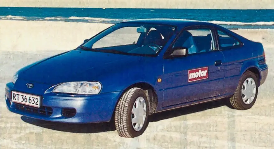 Niebieski Toyota Paseo stoi na plaży, z morzem w tle.