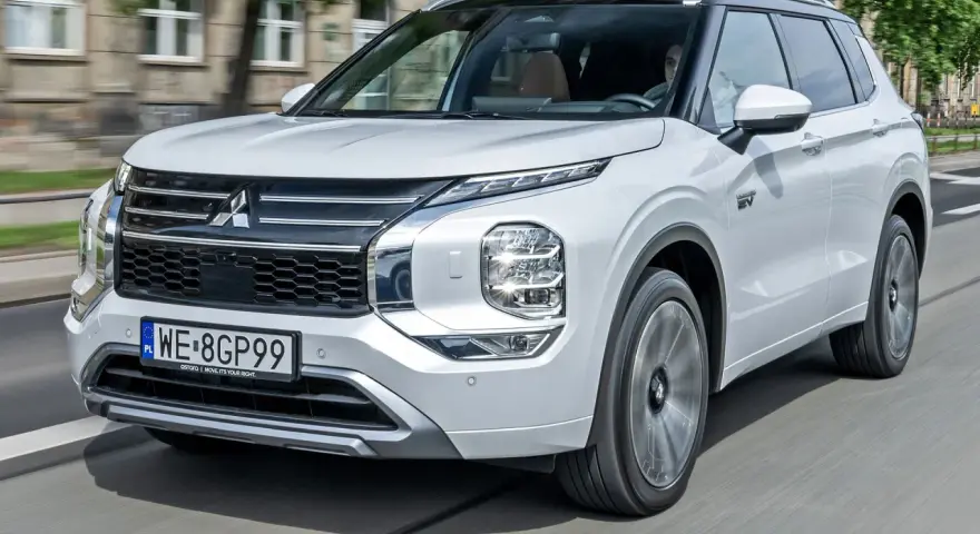 Biały Mitsubishi Outlander PHEV, jeden z nowoczesnych modeli tej marki, jedzie po mieście.