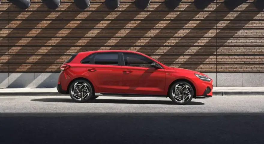 Czerwony Hyundai i30 stoi na tle ceglanej ściany z ciekawymi cieniami.