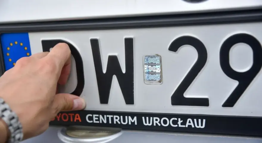 Dłoń zasłania literę "D" na tablicy rejestracyjnej DW 29. Widoczny hologram i napis "TOYOTA CENTRUM WROCŁAW".