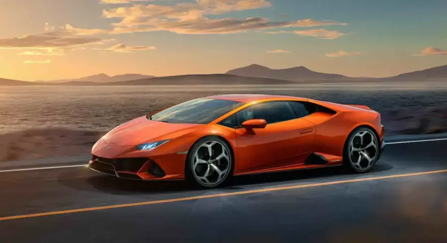 Pomarańczowy Lamborghini Huracan pędzi po pustej drodze nad jeziorem o zachodzie słońca.