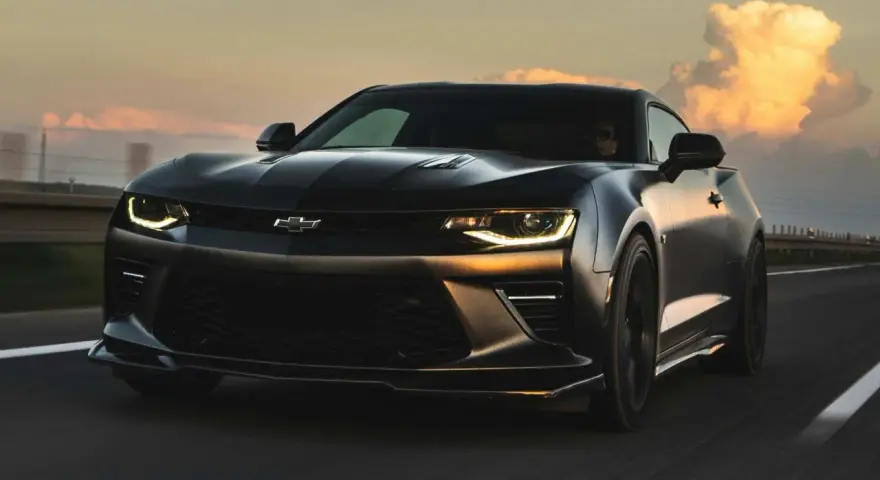 Czarny Chevrolet Camaro pędzi po autostradzie o zachodzie słońca.