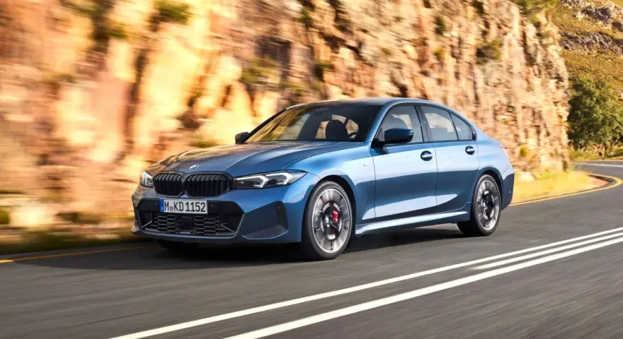 Niebieskie BMW klasy średniej jedzie po krętej drodze w skalistym krajobrazie.