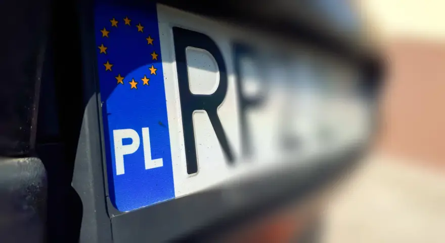 Zbliżenie na polską tablicę rejestracyjną z symbolem UE. Litery "PL" i fragment innych znaków sugerują, że pojazd jest w trakcie wyrejestrowania.