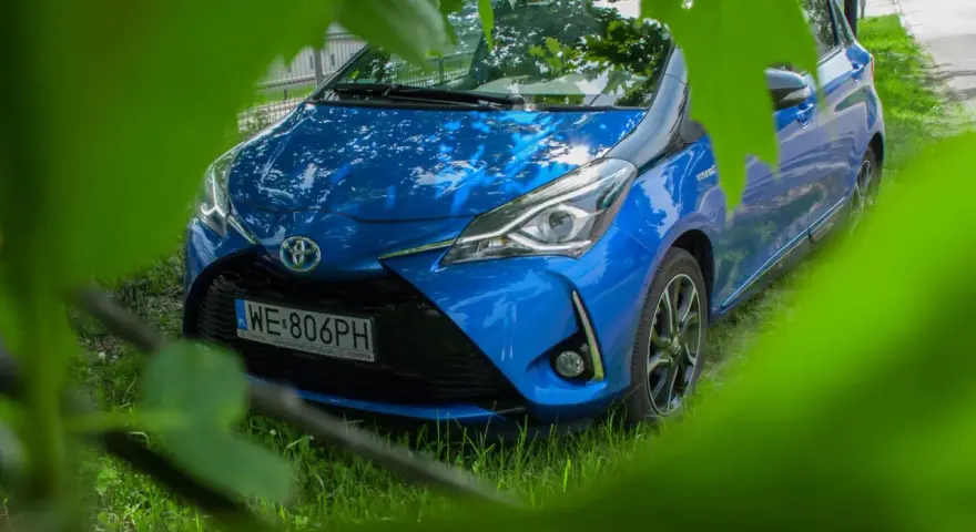 Niebieski Toyota Yaris Hybrid. Czy warto? Zobacz auto z bliska, ukryte wśród zieleni.