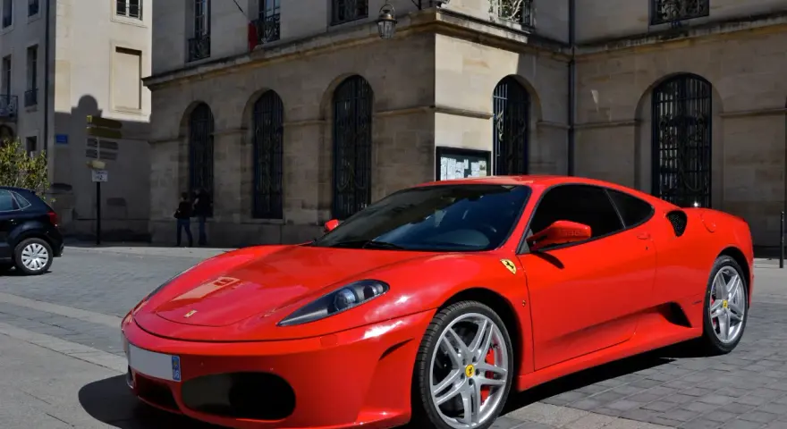 Czerwone Ferrari F430 na brukowanej ulicy przed kamienicą. Zastanawiasz się, ile kosztuje najtańsze Ferrari?