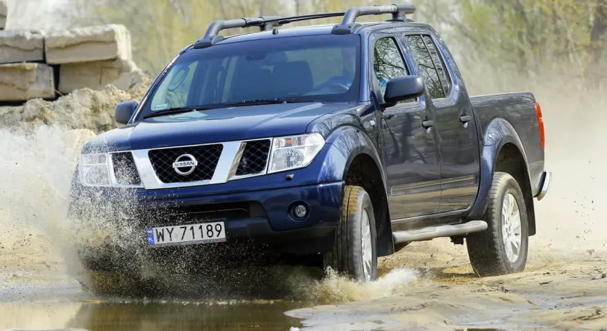 Niebieski Nissan Navara pokonuje wodną przeszkodę, wzbijając fontanny błota.