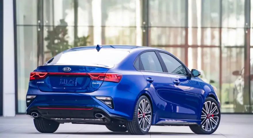 Niebieskie Kia Forte GT z czerwonymi akcentami, zaparkowane przed nowoczesnym budynkiem.