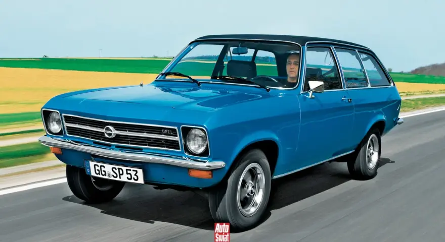 Niebieski Opel Ascona w wersji kombi jedzie po drodze, za nim pola i niebo.
