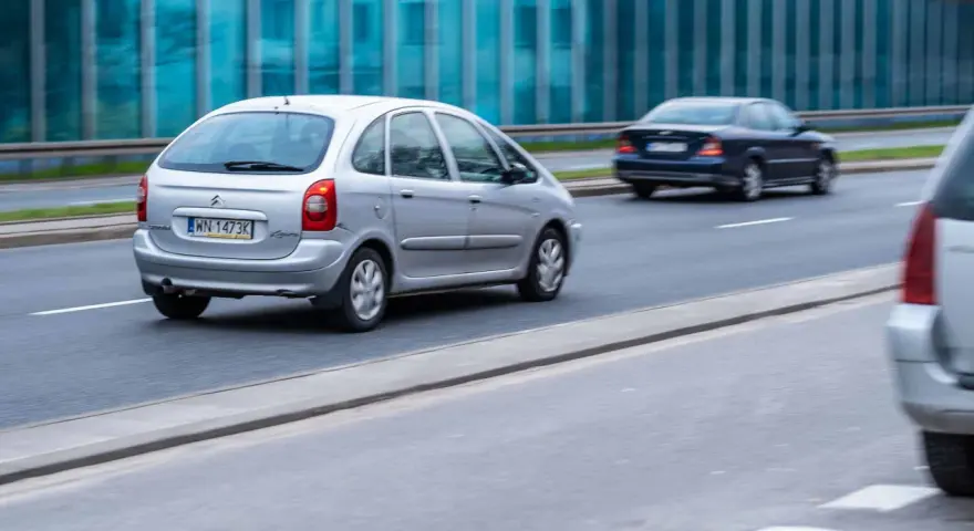 Srebrny Citroën Xsara Picasso jedzie po drodze, mijając inne samochody.