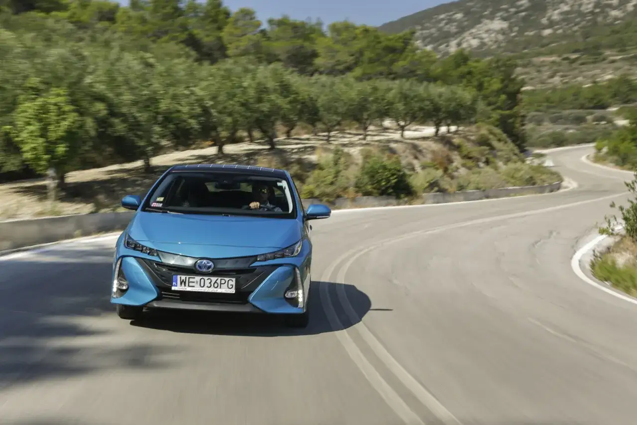 Niebieska Toyota Prius pokonuje kręty górski zakręt. Zastanawiasz się, ile pali Toyota Prius? Ten model jest znany z niskiego spalania.