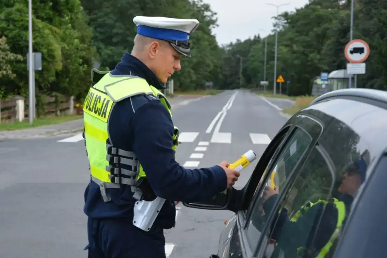 Policjant kontroluje kierowcę alkomatem. Jazda po alkoholu to poważne wykroczenie.