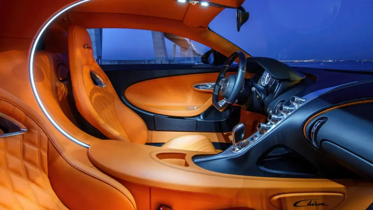 Wnętrze Bugatti Chiron: pomarańczowa skóra, karbon, eleganckie detale. Luksus i moc w każdym calu.
