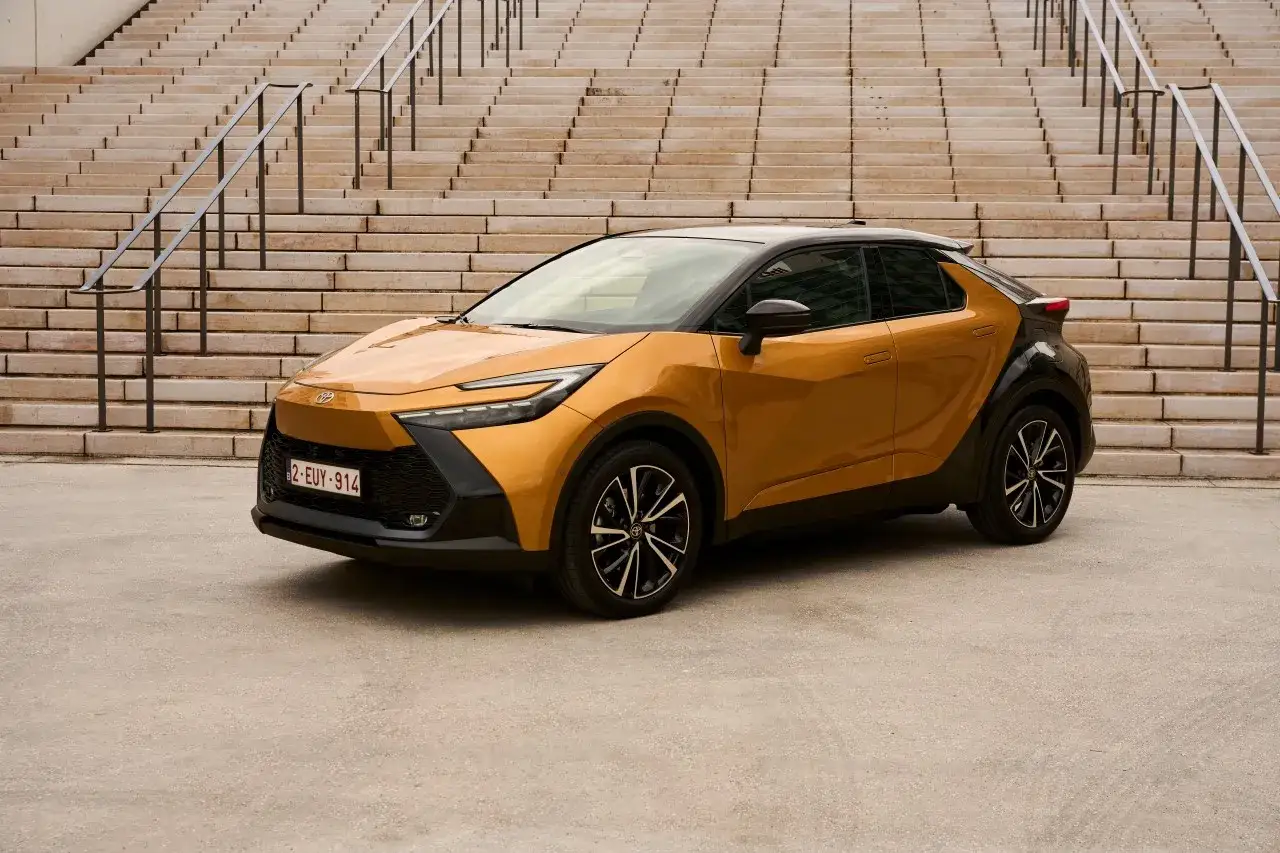 Złoty Toyota C-HR hybryda czy benzyna? Stylowy crossover z czarnymi akcentami na tle schodów.