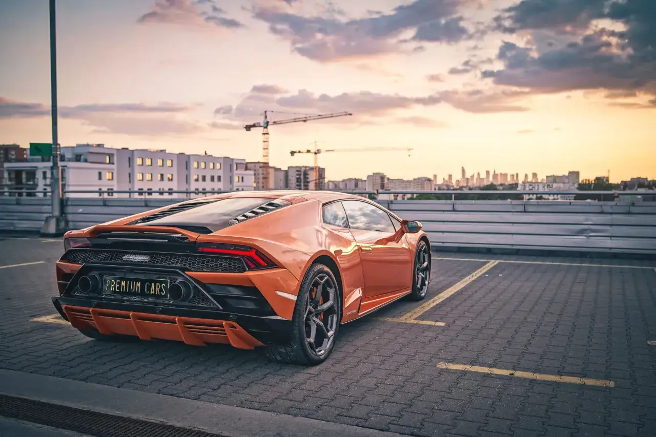 Pomarańczowe Lamborghini na parkingu, zachód słońca. Zastanawiasz się, ile kosztuje wypożyczenie lamborghini?