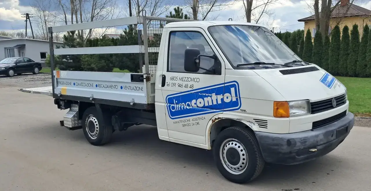 Biały Volkswagen Transporter z zabudową skrzyniową, idealny jako tani bus do 10 tys. zł. Na drzwiach logo 