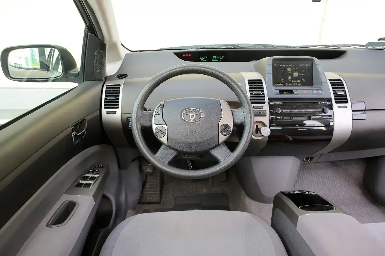 Wnętrze Toyoty Prius. Czy warto kupić ten hybrydowy samochód? Kierownica, deska rozdzielcza z ekranem i radiem.